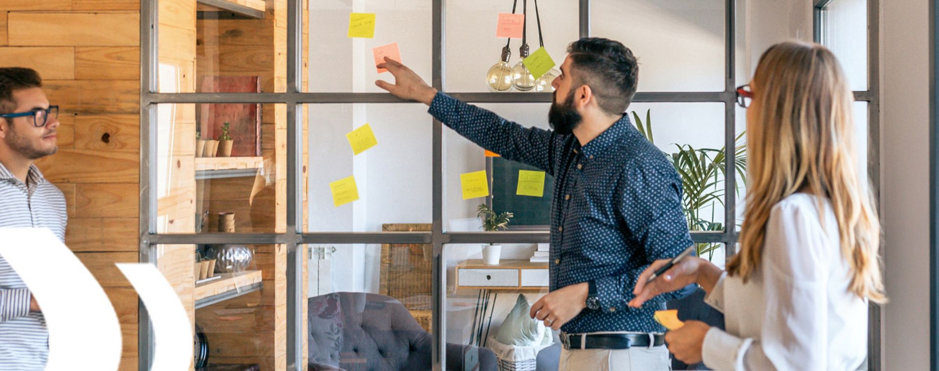 Personen kleben Post-its an eine Fensterwand, symbolisieren interaktive Live-Schulungen, die online oder vor Ort stattfinden.