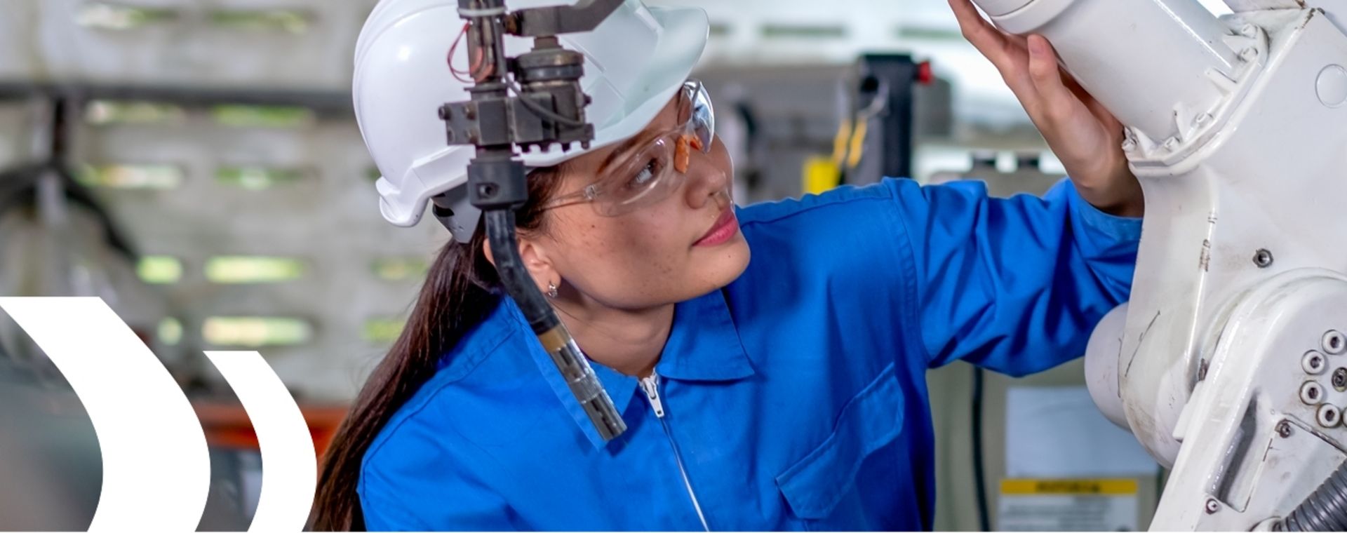 Frau mit Schutzbrille und Helm prüft ein Gerät, symbolisiert die Ausbildung zur Qualitätssicherung mit Fokus auf Prüfmethoden und Qualitätsprüfung.